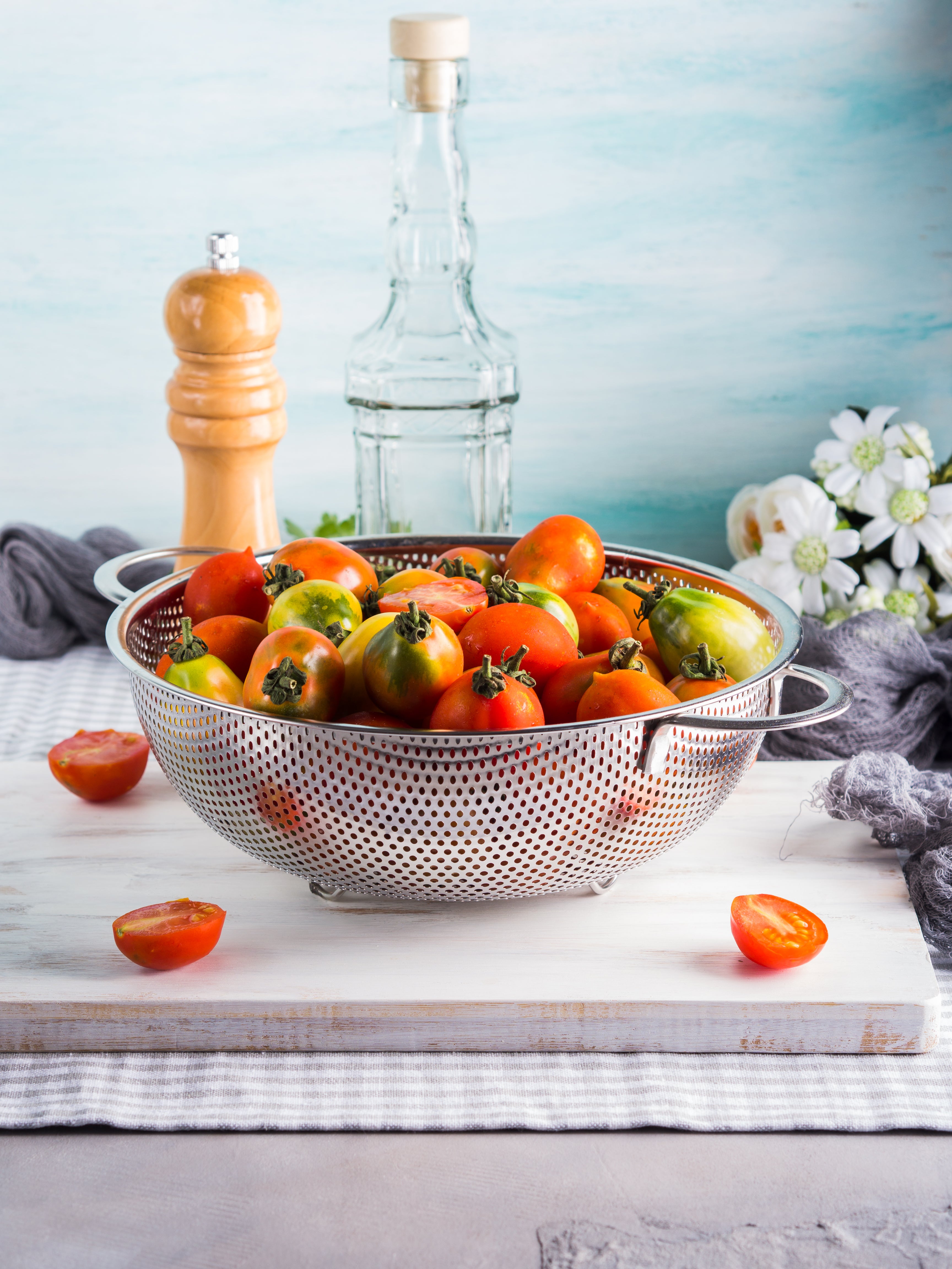 Metal colander with tomatoes on a white surface with a blue gradient background