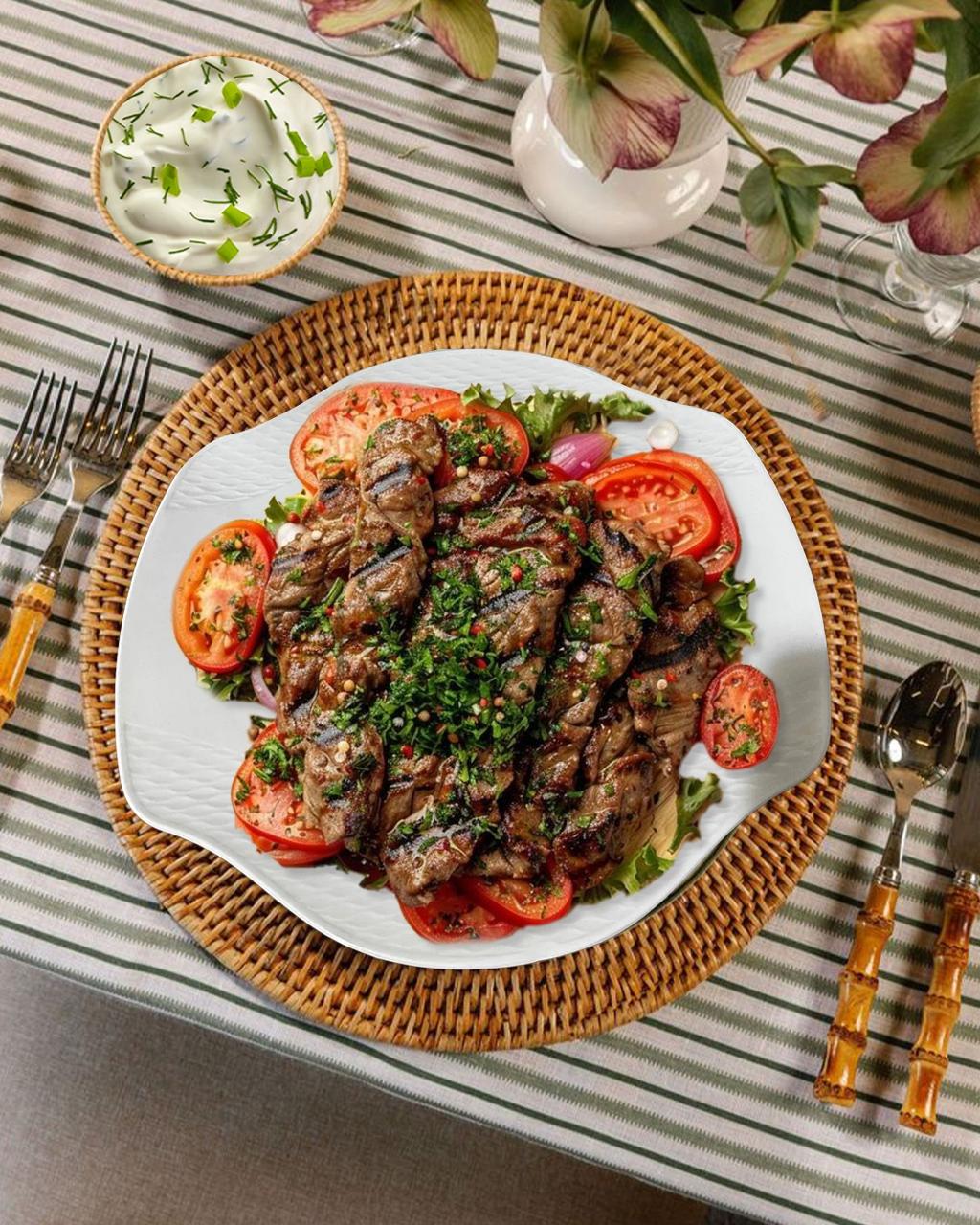 lated dish of grilled meat with vegetables on a striped tablecloth